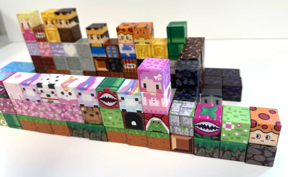 A variety of colorful cube toys with pixelated designs resembling characters and patterns are stacked in rows on a white surface, offering a perfect early finisher idea for creative play.