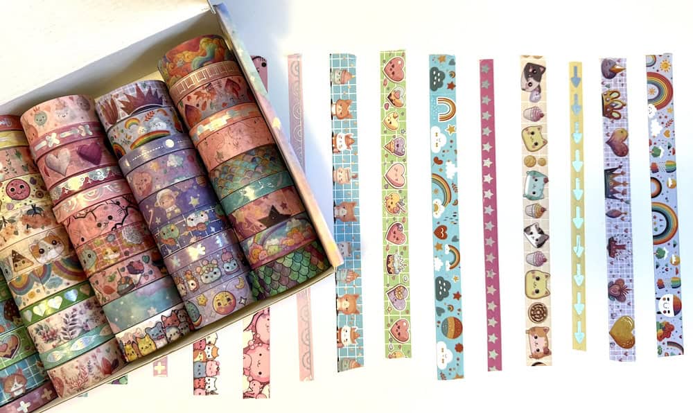 A collection of colorful washi tape rolls in a box, with various patterns including hearts, animals, and stars, next to cut strips arranged in rows on a white background.