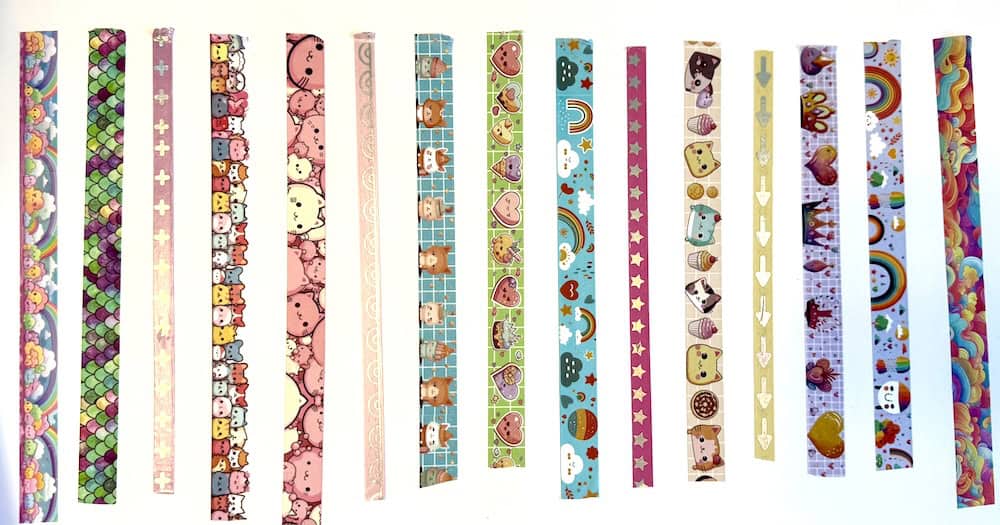 An array of decorative washi tapes with various patterns and colors, featuring cartoon animals, rainbows, and geometric designs, arranged vertically on a white background.