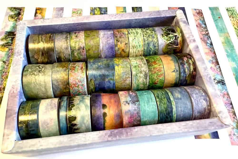 A box filled with rows of decorative washi tapes in various pastel colors and nature-themed patterns.